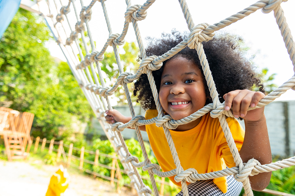 bright-futures-wide A young black girl smiles while climbing rope ladder